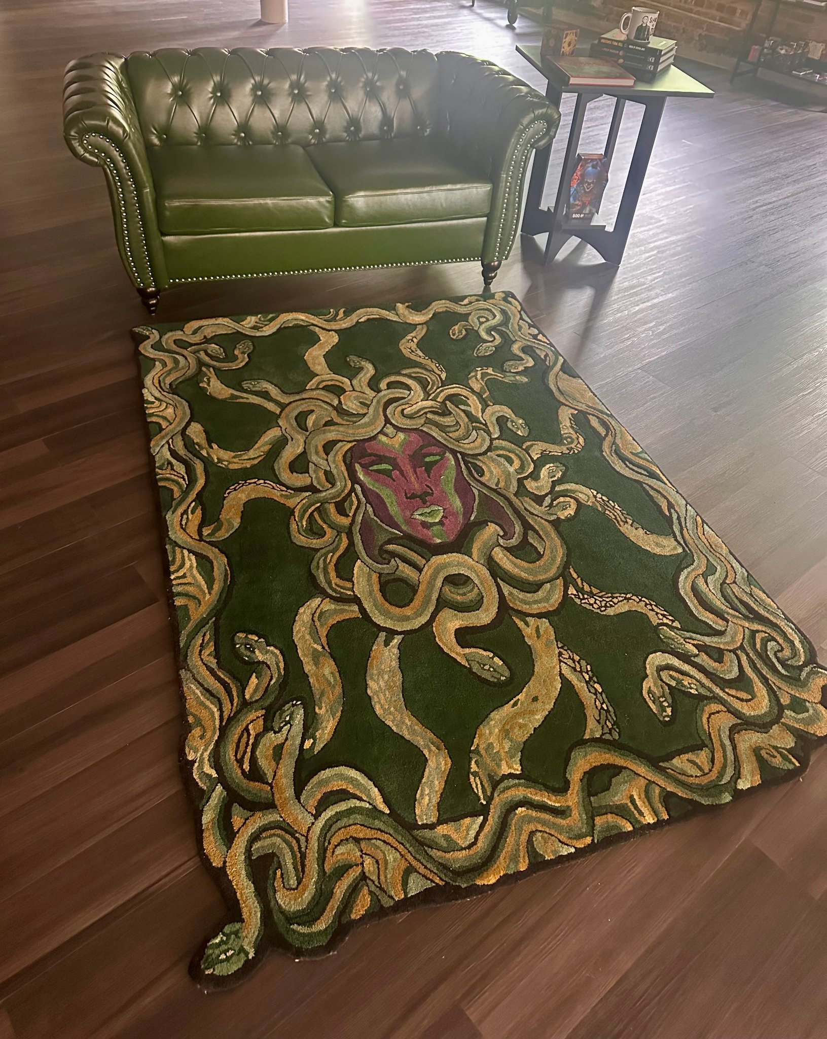 Hand-tufted Medusa rug with golden serpents on deep green, beside the green leather Chesterfield sofa