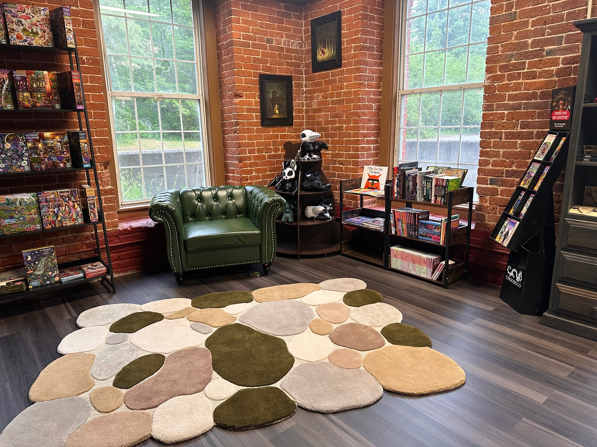 Bright corner reading nook with green leather Chesterfield armchair, exposed brick walls, and puzzle shelves